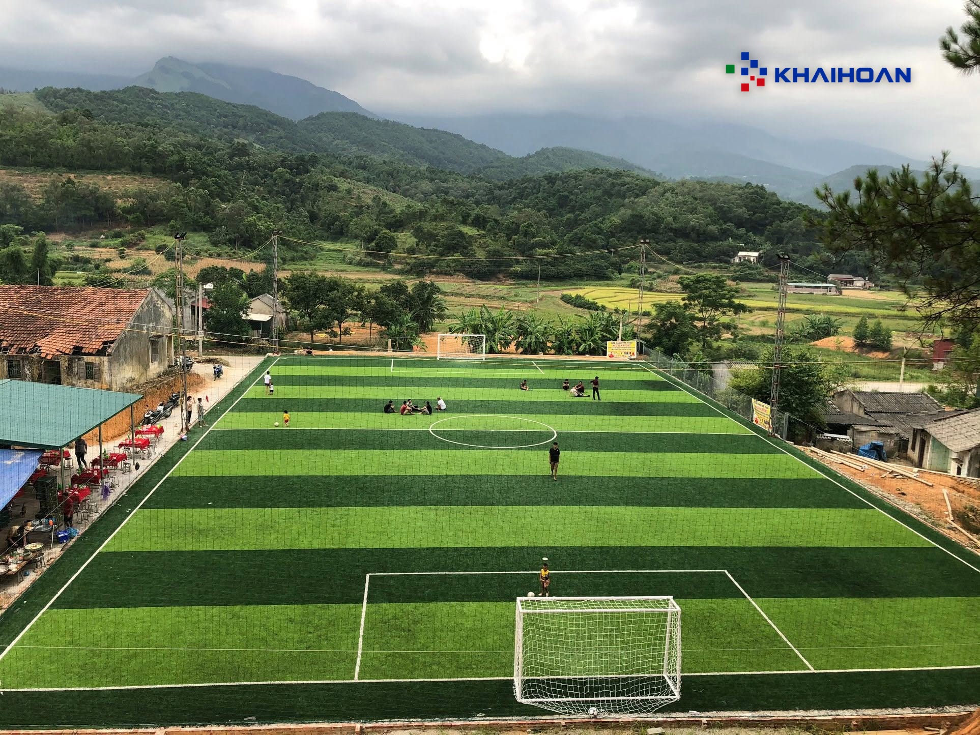 Sân cỏ nhân tạo giữa khu dân cư vùng núi, nhìn từ trên cao ban ngày